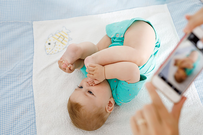 父母用智能手机给宝宝拍照。萌萌的新生宝宝把脚放在嘴里