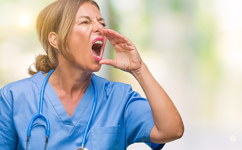 中年资深护士女医生隔着孤立的背景大声喊叫和尖叫，一边用手捂着嘴。通信的概念。