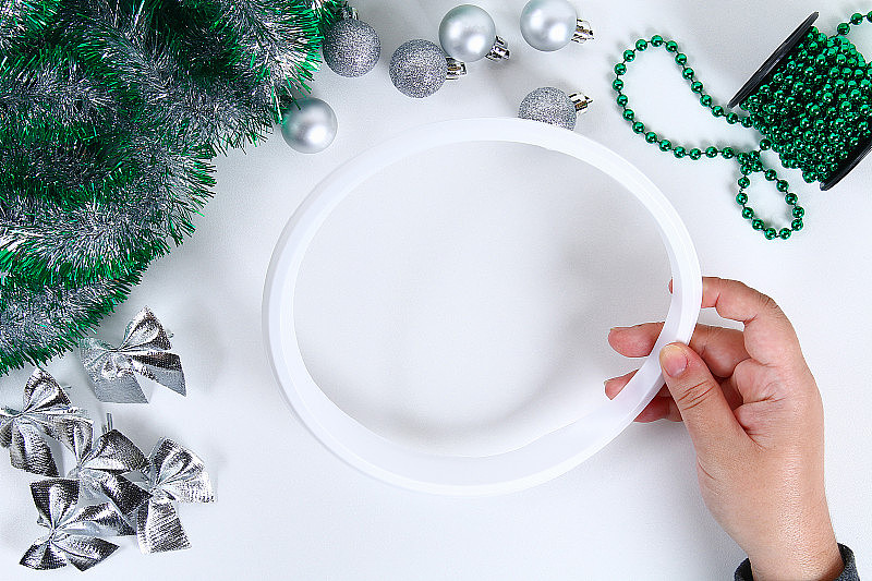 自制圣诞花环。教你如何用塑料盘、金属丝、珠子、蝴蝶结和球亲手制作圣诞花环。手工制作的装饰。银绿色的花环。前视图。