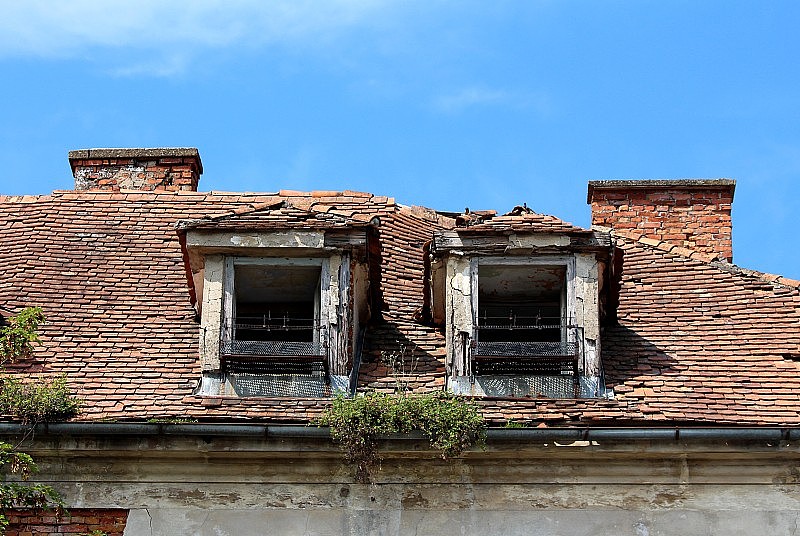 在废弃的旧建筑上，两扇被毁的屋顶窗户和生锈的金属花架，屋顶瓦片破碎和缺失