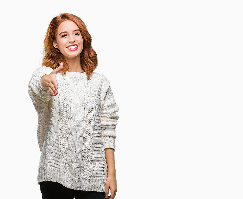 年轻美丽的女人在孤立的背景穿着冬季毛衣微笑友好地提供握手作为问候和欢迎。成功的事业。