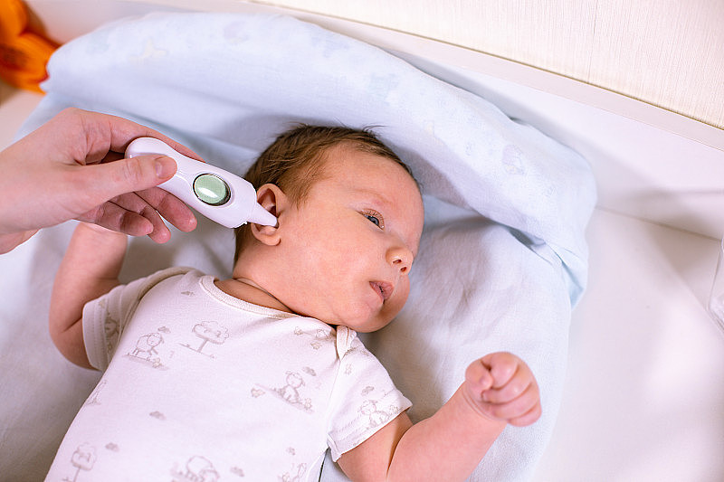 用非接触式体温计测量宝宝体温。妈妈用耳朵里的温度计测量宝宝的体温