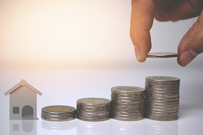房产投资和房屋抵押的理财理念，手把钱和房屋硬币叠在一起