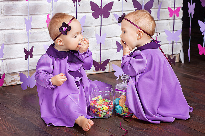 一岁的双胞胎生日。可爱的双胞胎姐妹庆祝一岁生日。双胞胎小女孩坐在地板上吃糖果