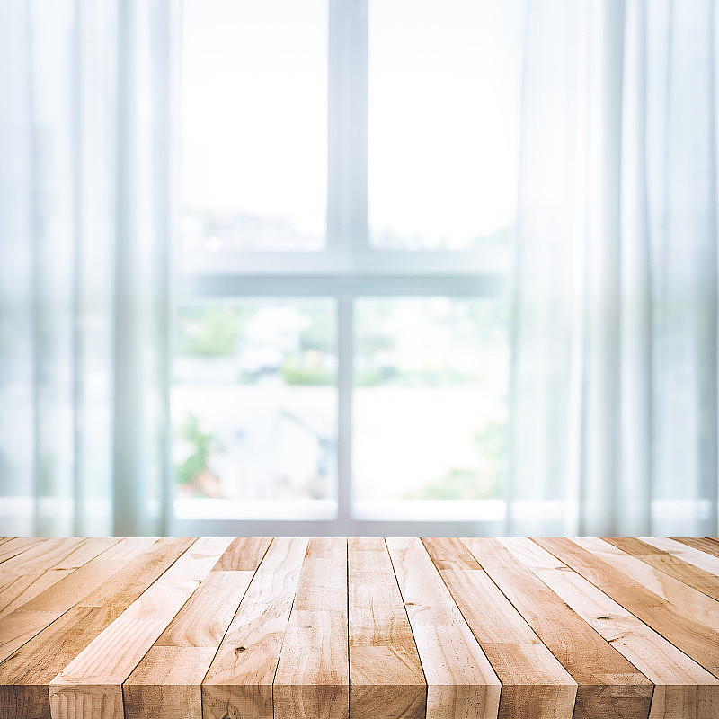空的木质桌面上模糊的白色窗帘与窗户的视图背景