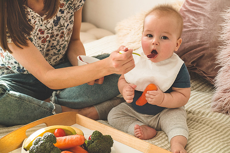 首先是给小孩子吃固体食物。新鲜有机胡萝卜作为午餐蔬菜。婴儿断奶。妈妈和小男孩吃蔬菜