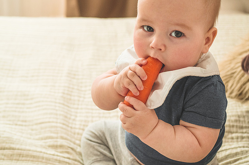 首先是给小孩子吃固体食物。新鲜有机胡萝卜作为午餐蔬菜。婴儿断奶。妈妈和小男孩吃蔬菜