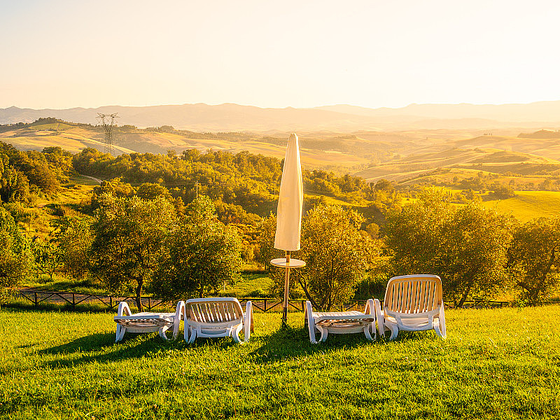 托斯卡纳风景中的美丽的休息场所，有雨伞和日光浴床。夏天晚上日落。意大利