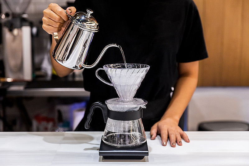 女咖啡师用另一种叫做滴式的方法来制作倒式咖啡。咖啡研磨机，咖啡架和倒在大理石台面上。