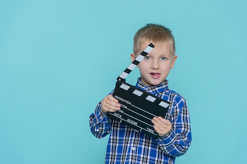 微笑的孩子拿着电影拍板在蓝色的背景