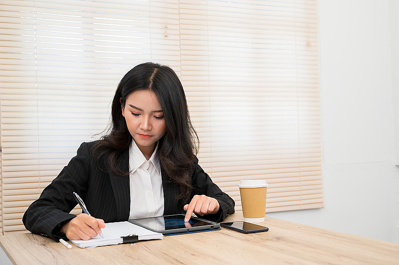 亚洲职业女性穿着黑色套装坐在办公桌前。
