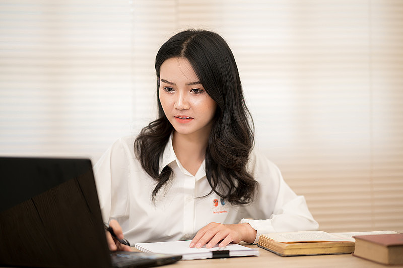 亚洲女性穿着白衬衫坐在办公桌前。