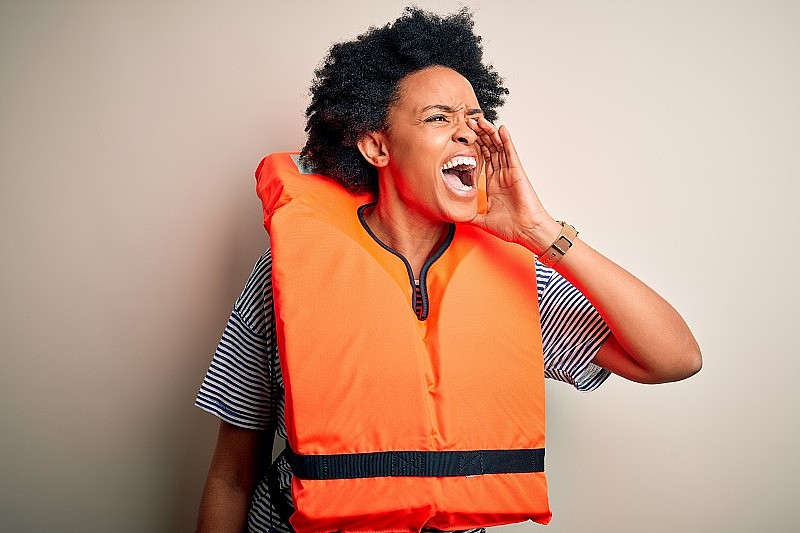 年轻的非洲裔美国妇女卷发穿着橙色的保护救生衣大声喊叫和尖叫，用手捂着嘴。通信的概念。