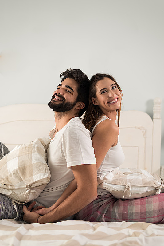 年轻幸福的夫妇在他们的卧室里背靠背放松
