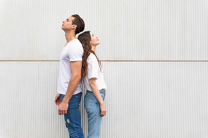 一对年轻夫妇背靠背地站在白色的城市墙壁上