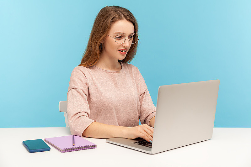 戴着书呆子眼镜的聪明女人在笔记本电脑上打字，在办公室里用聪明勤奋的表情工作。学生学习