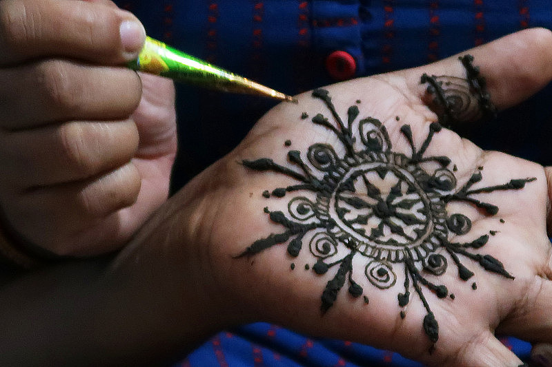 不认识的人在新郎的手上绘制指甲花/曼海蒂粘贴纹身设计，这是印度次大陆的婚礼传统，被称为曼海蒂仪式，为新娘和新郎带来积极的精神，健康，繁荣。