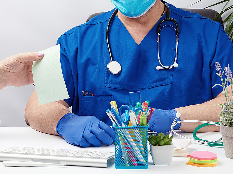 身穿蓝色制服，戴着乳胶手套的医生坐在一张白色的桌子前，领着一个病人接待处
