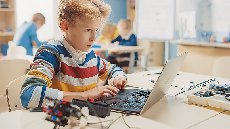 小男孩用笔记本电脑为机器人工程课编写软件。小学科学教室，有天赋的聪明的孩子与技术工作