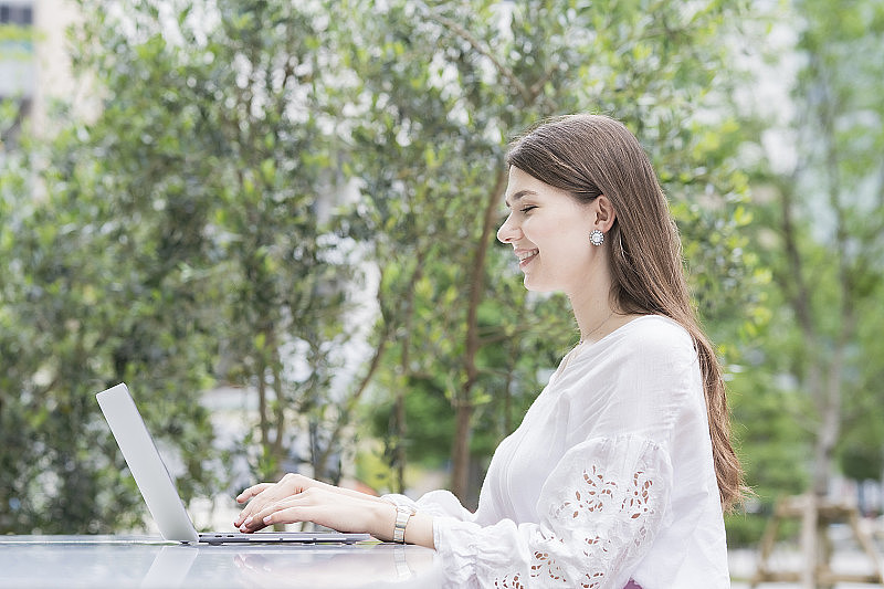 一个在户外操作笔记本电脑的年轻女商人