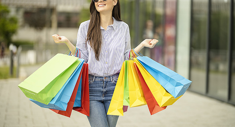不可辨认的快乐女人拿着购物袋在购物中心享受购物