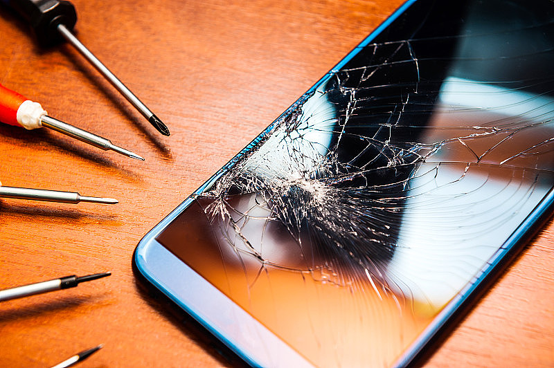 一个破碎的手机和一个破碎的屏幕，还有工具，螺丝刀放在木桌上。电子产品维修店。