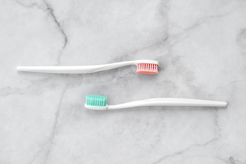 大理石背景上的两支牙刷，刷毛分别为粉色和蓝绿色。牙科和保健概念。俯视图，平放。