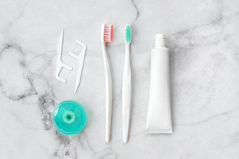 一套粉色和绿松石蓝色牙刷，牙膏和其他工具的大理石背景。牙科和保健概念。俯视图，平放。