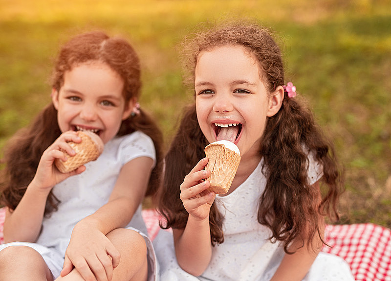 快乐的双胞胎女孩在公园吃冰淇淋