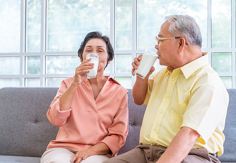 两对老年夫妇在沙发客厅里喝着牛奶，享受着退休养生和健康生活理念。