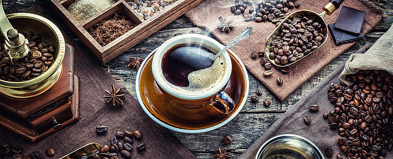 一杯芳香的黑咖啡，一个咖啡研磨机，一个咖啡机，桌上放着不同品种的咖啡豆。