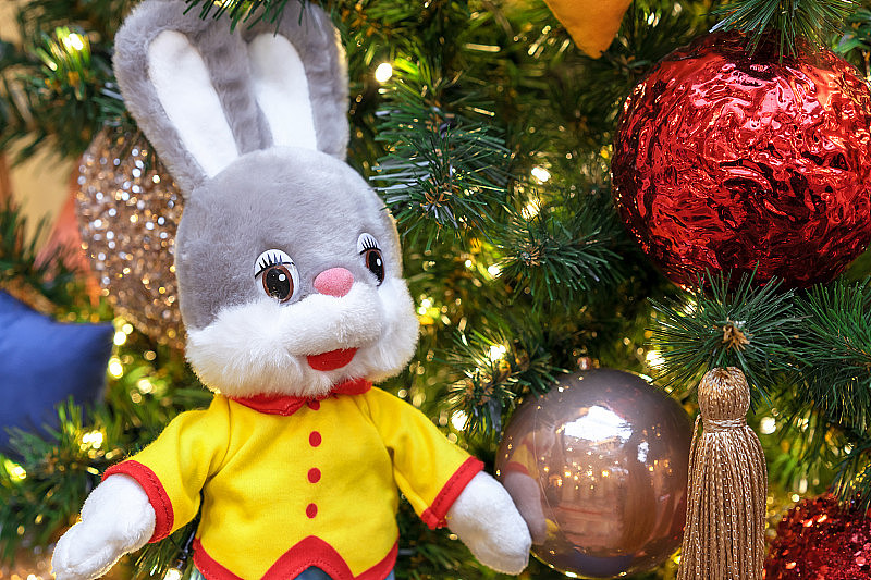 在装饰过的圣诞树的背景上有一只长耳朵的兔子的软玩具。