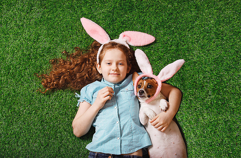 可爱的卷发女孩和长着兔子耳朵的胖狗