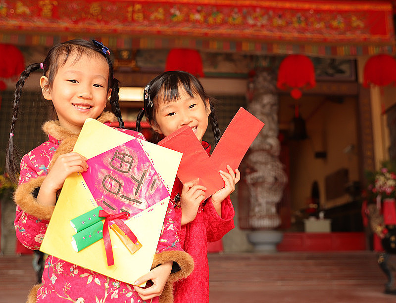 两个亚洲双胞胎女孩穿着旗袍在寺庙前进行新年访问。