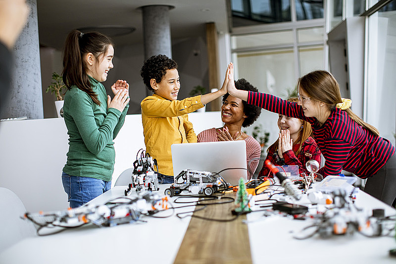快乐的孩子们和他们的非裔美国女科学老师一起用笔记本电脑编程机器人教室里的电动玩具和机器人
