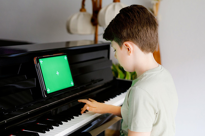 学校男孩学习弹钢琴平板应用程序。孩子有乐趣与学习弹奏乐器。带有绿色屏幕色度键背景的平板电脑，用于新应用程序，商务和程序