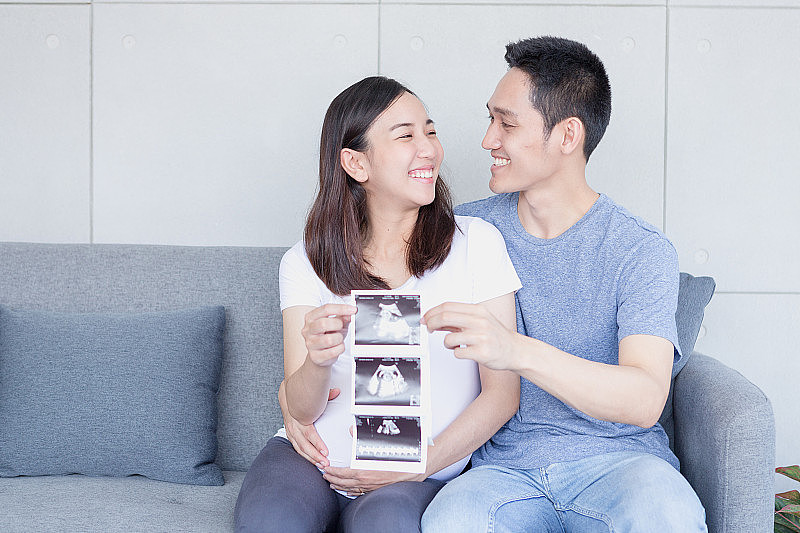 超声波怀孕的妈妈和爸爸。开心的孕妇带着丈夫展示自己宝宝的扫描图。幸福的夫妇正拿着宝宝的超声波照片。