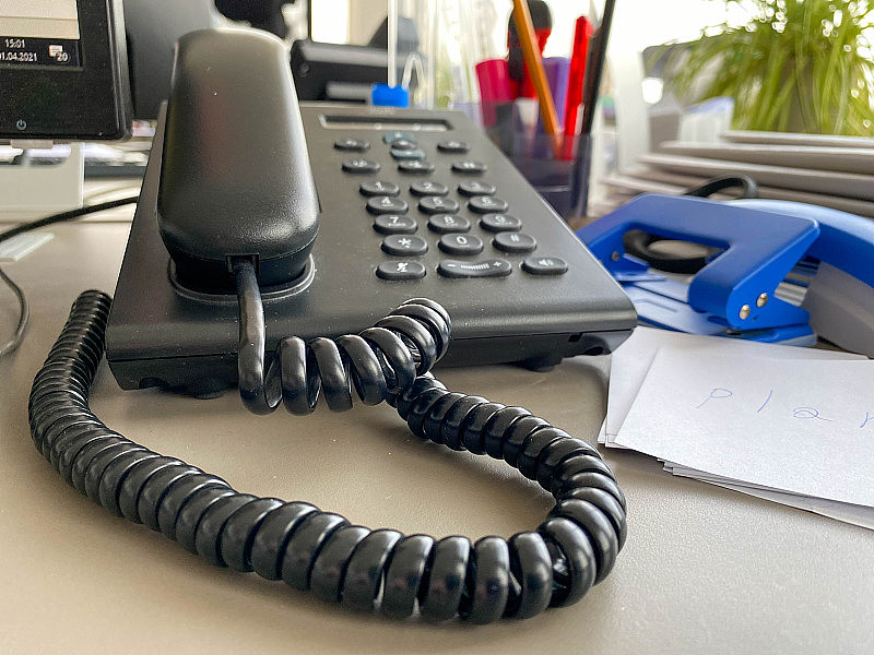 黑色的固定电话，一个管子，按钮和电线在办公桌的工作桌上和办公用品。业务工作