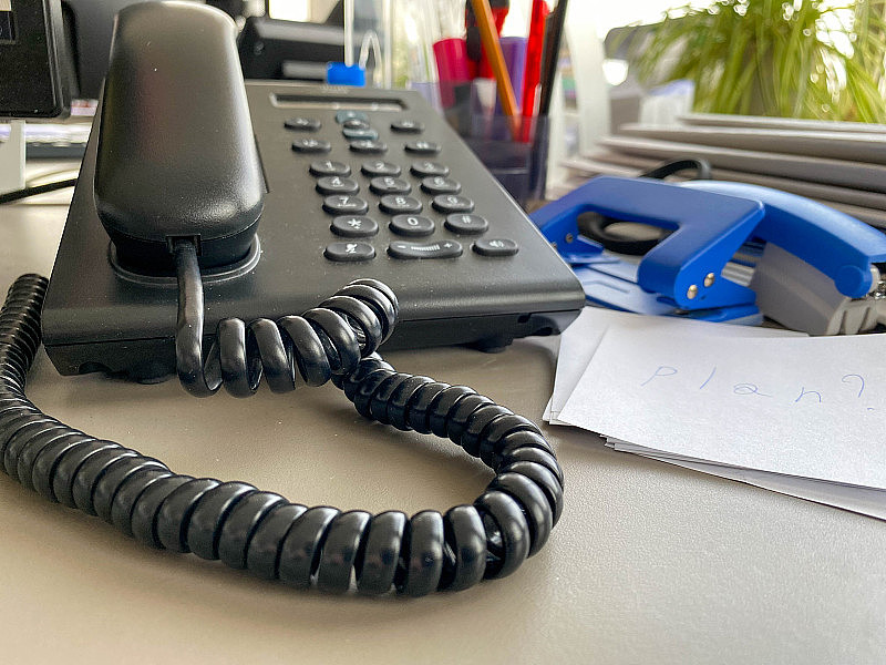 黑色的固定电话，一个管子，按钮和电线在办公桌的工作桌上和办公用品。业务工作