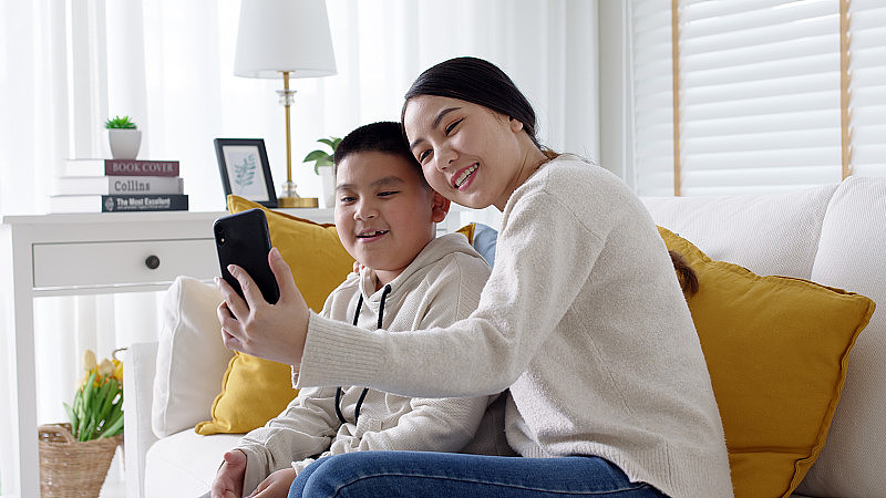 视频电话电话会议亚洲家庭与年轻的母亲和儿子使用移动电话、互联网、wifi在家中客厅远程聊天，在自我隔离中感受快乐。