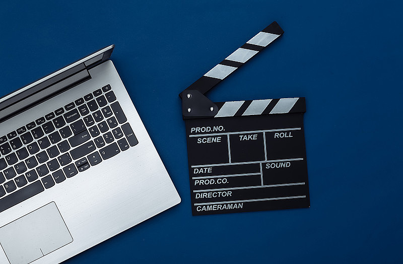 电影拍板与笔记本电脑在经典的蓝色背景。电影制作，电影制作，网络电影。俯视图