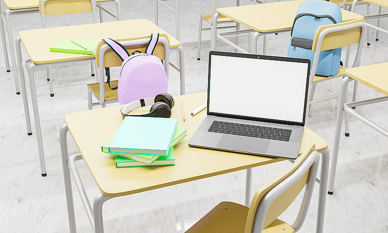 笔记本电脑放在教室的课桌上，周围有书籍和用品