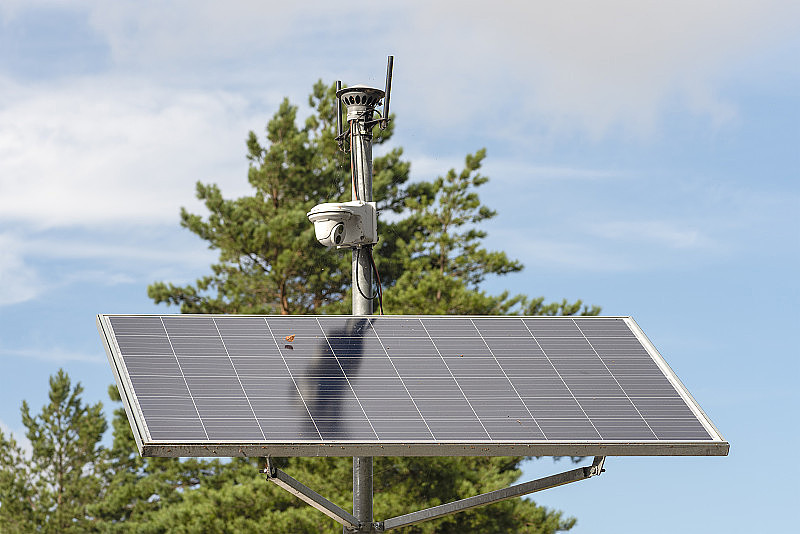 太阳能监控摄像头。在蓝天的背景下，为城市公园的监控摄像头供电的太阳能电池板。安全清洁能源理念