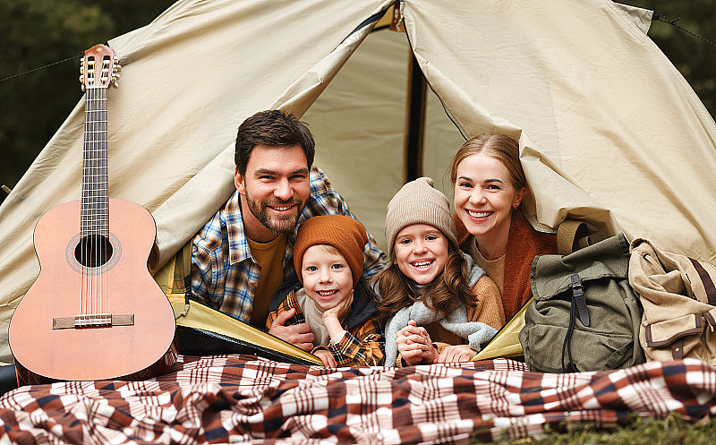 幸福的家庭爸爸、妈妈和两个小孩坐在森林营地的帐篷里