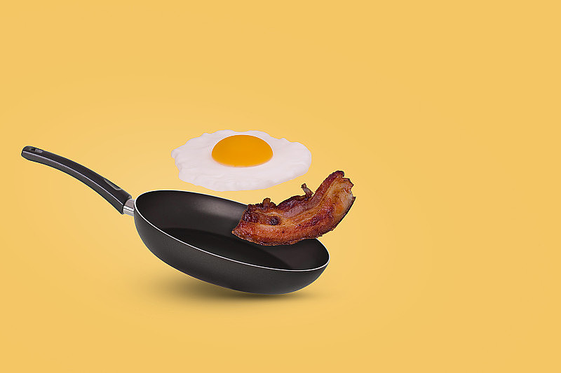 用一个煎锅，一个煎蛋和熏肉在黄色背景上，这是最简单的想法。创新食品的概念。