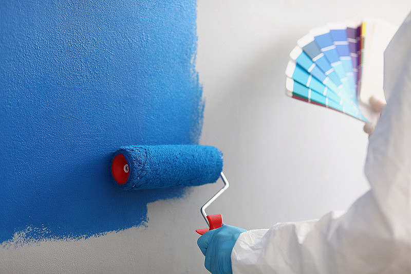 油漆工用画笔工具涂上蓝色的彩绘墙，现场工人