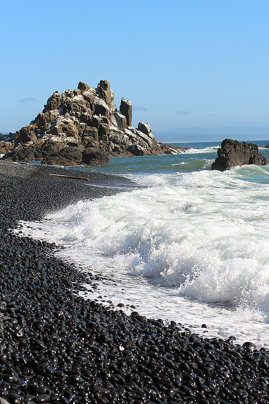 俄勒冈州海岸的雅奎纳头灯塔风景区，海浪撞击着鹅卵石海滩的岩石