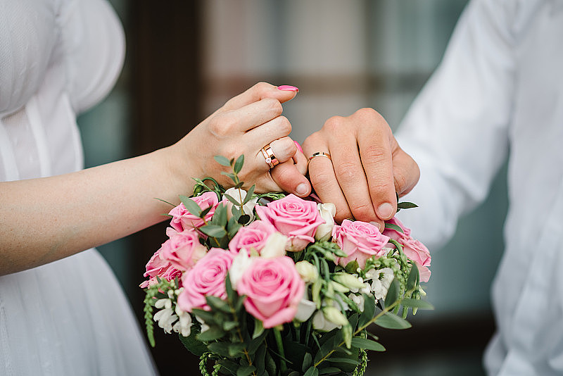 新婚夫妇手上的结婚戒指。裁剪图像的新娘和新郎交叉小手指的花束背景。承诺的概念。十指相扣，许下诺言。誓言。