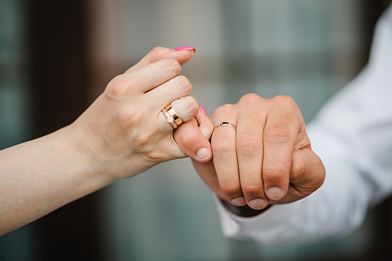 新婚夫妇手上的结婚戒指。承诺的概念。裁剪的女人和男人交叉小手指在灰色背景孤立的图像。十指相扣，许下诺言。誓言。
