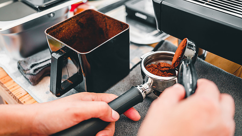 特写咖啡师在咖啡研磨机旁将现磨咖啡豆倒入滤器中为顾客制作咖啡